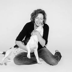 Bio black and white photo of Amy Buttry, smiling and hugging a large black an white dog